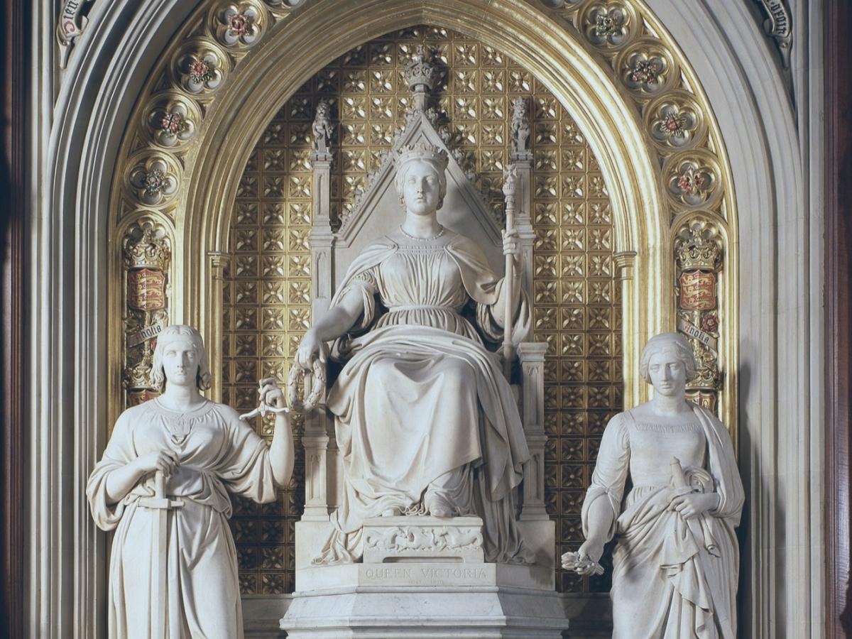 Under a gilded arch, a statue of a young Queen Victoria sits, between two standing figures.