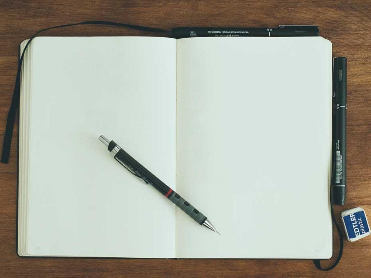 A notebook is open at two blank pages. a pen rests across the page.s.