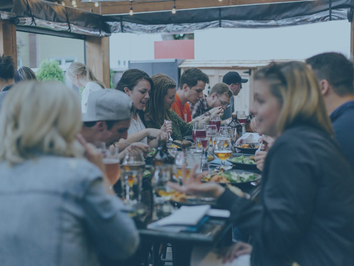 A large group of friends sit at a crowded table and share a meal together.