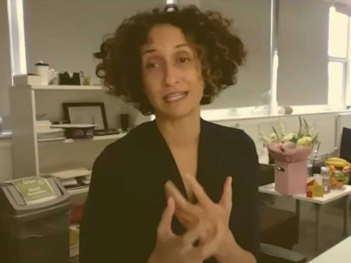 A head teacher sits at her desk, holding her hands in a gesture in front of her.