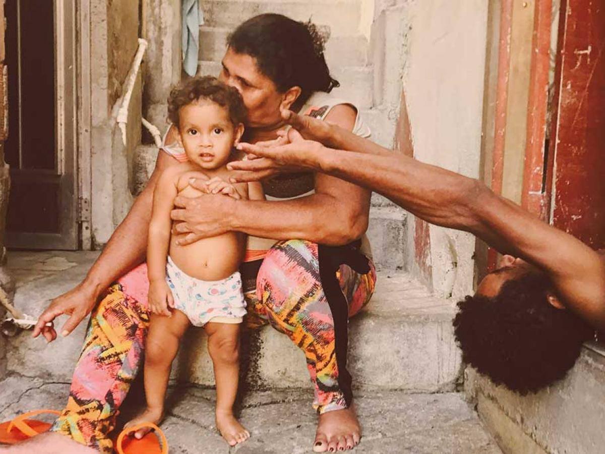 A mother sits with a toddler standing in front of her. The father appears from the side lying on his back reaching an arm out.