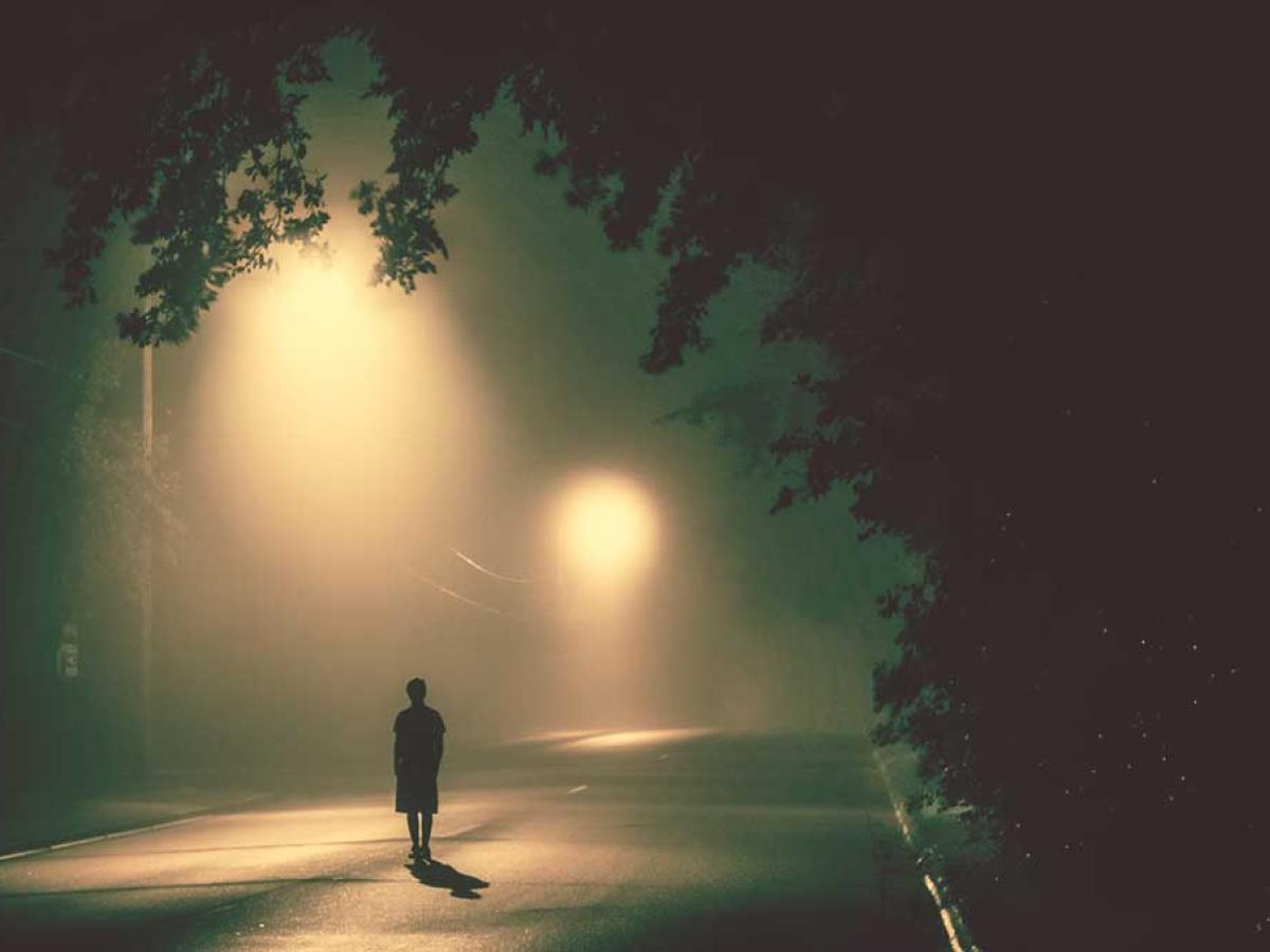 A person stands in a road under misty street lights.