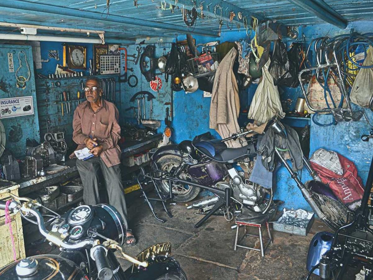 A mechanic stands in a workshop beside a motorcycle under repair.