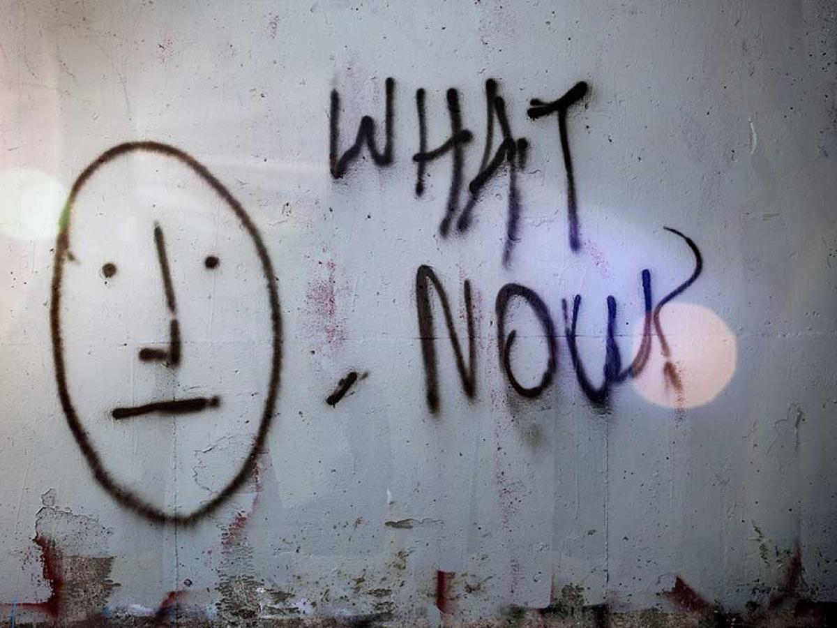 A graffited wall shows a stick man face next to 'what now'