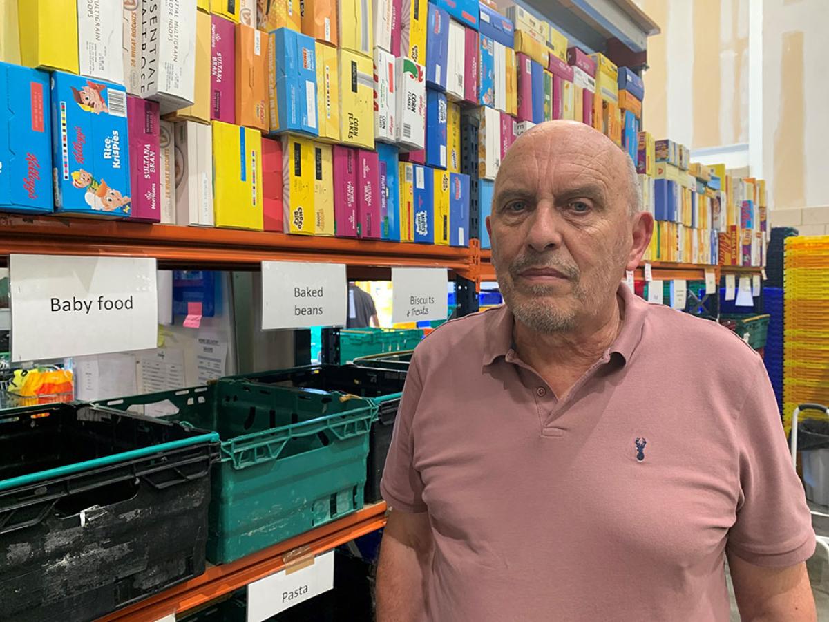 A man stands in front of a food bank's shelves of cereals and boxes labelled by foot type.