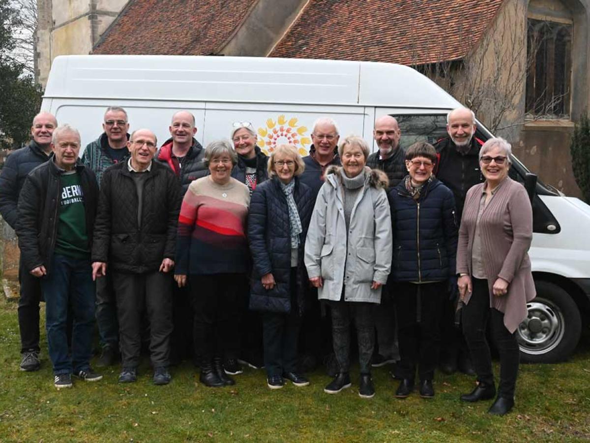 A group of people stand in front of the side of a van marked 'Furniture Friends.