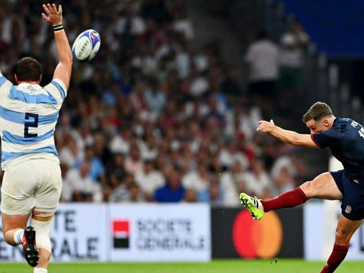 A rugby ball sails towards a player in a striped jersey from the foot of a kicker who has a leg and an arm extended out.