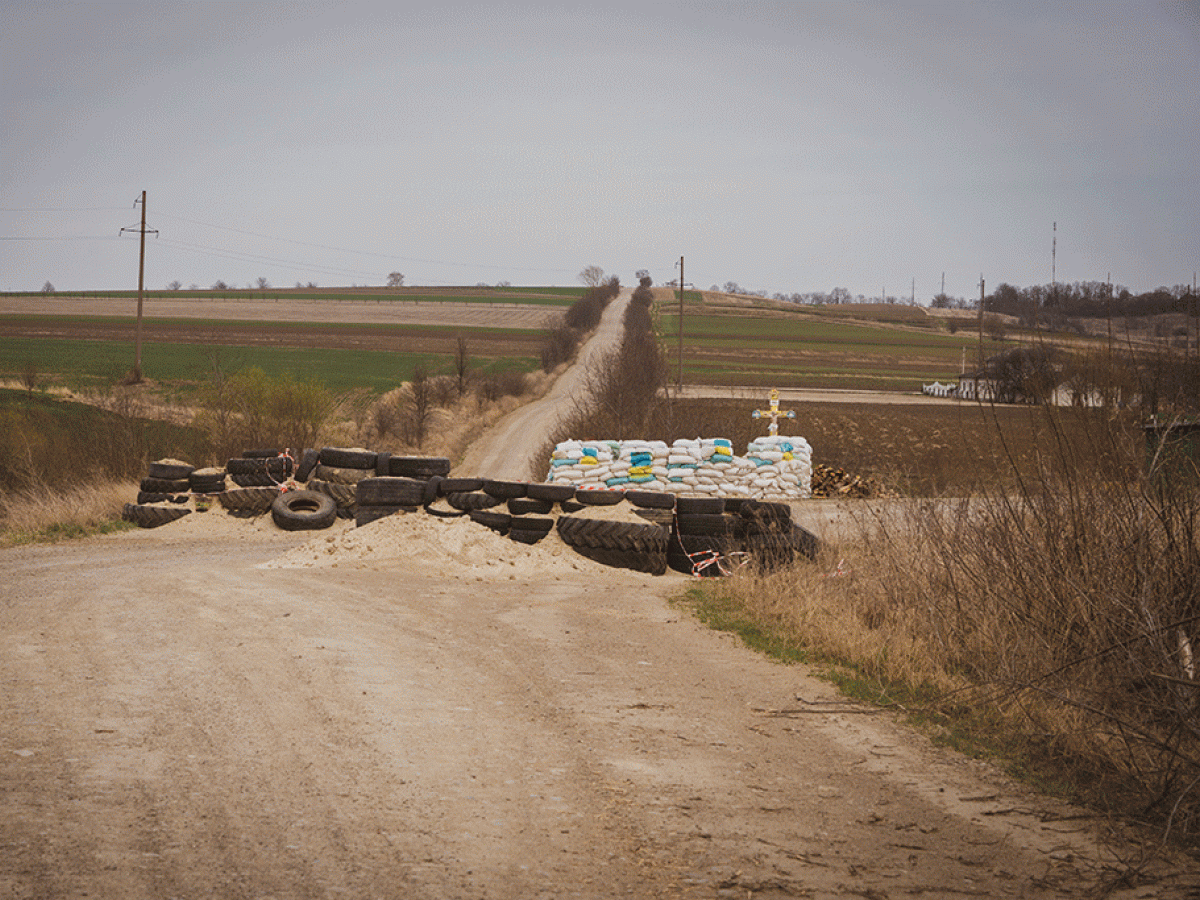 a dirt barricade blocks a cross roads, behind which stands a roadside cross