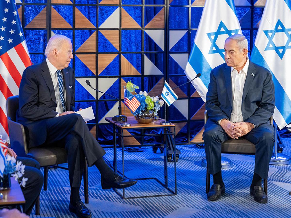 Two country leaders sit in chairs next to each other with their country's flags behind