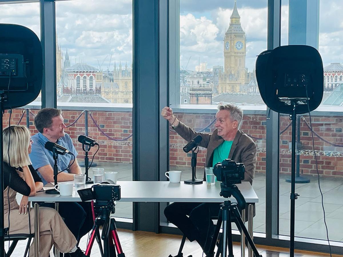 At a podcast recording in a room overlooking Big Ben, A man holds his hand up in gesture while speaking