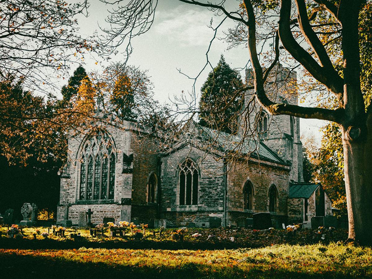 An autumnal scene of a church yard and church framed by leafless trees.