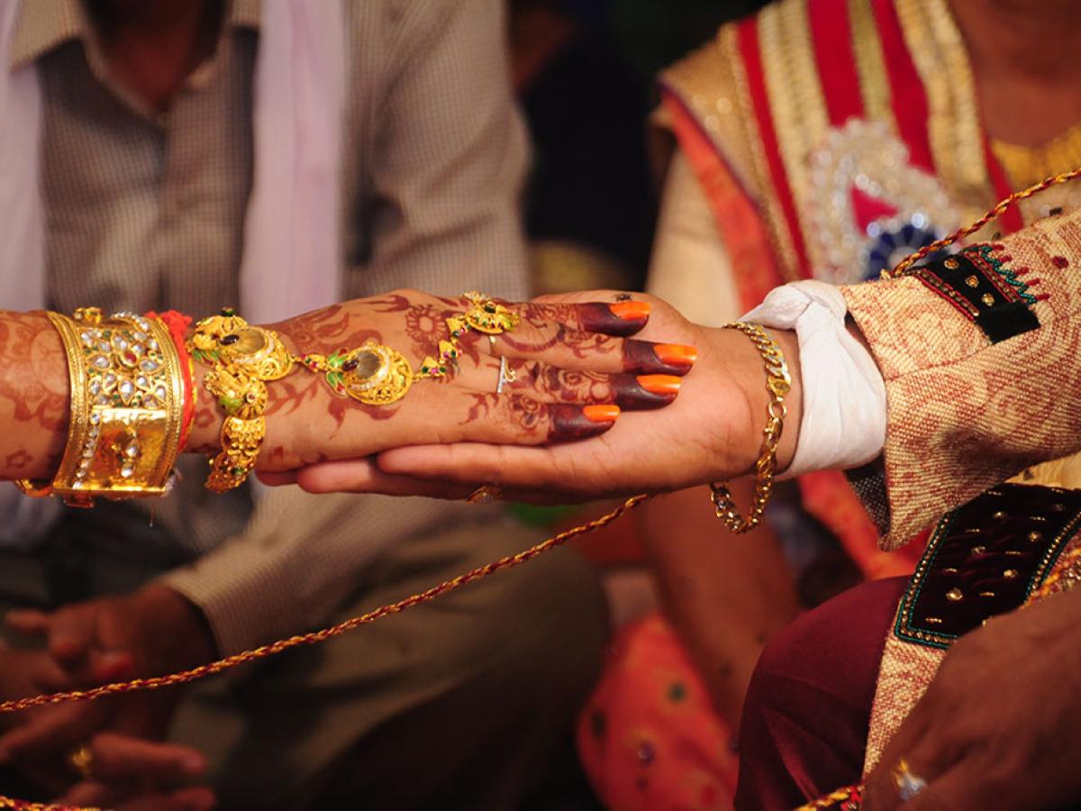 A close-up of a bride groom holding the brides hand. Her hand is henna tattooed and bears gold rings and bracelets. 