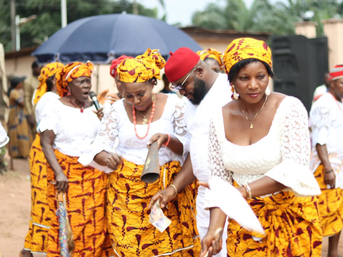 A group of women stand and dance at a celebration in the street, wearing matching skirts..