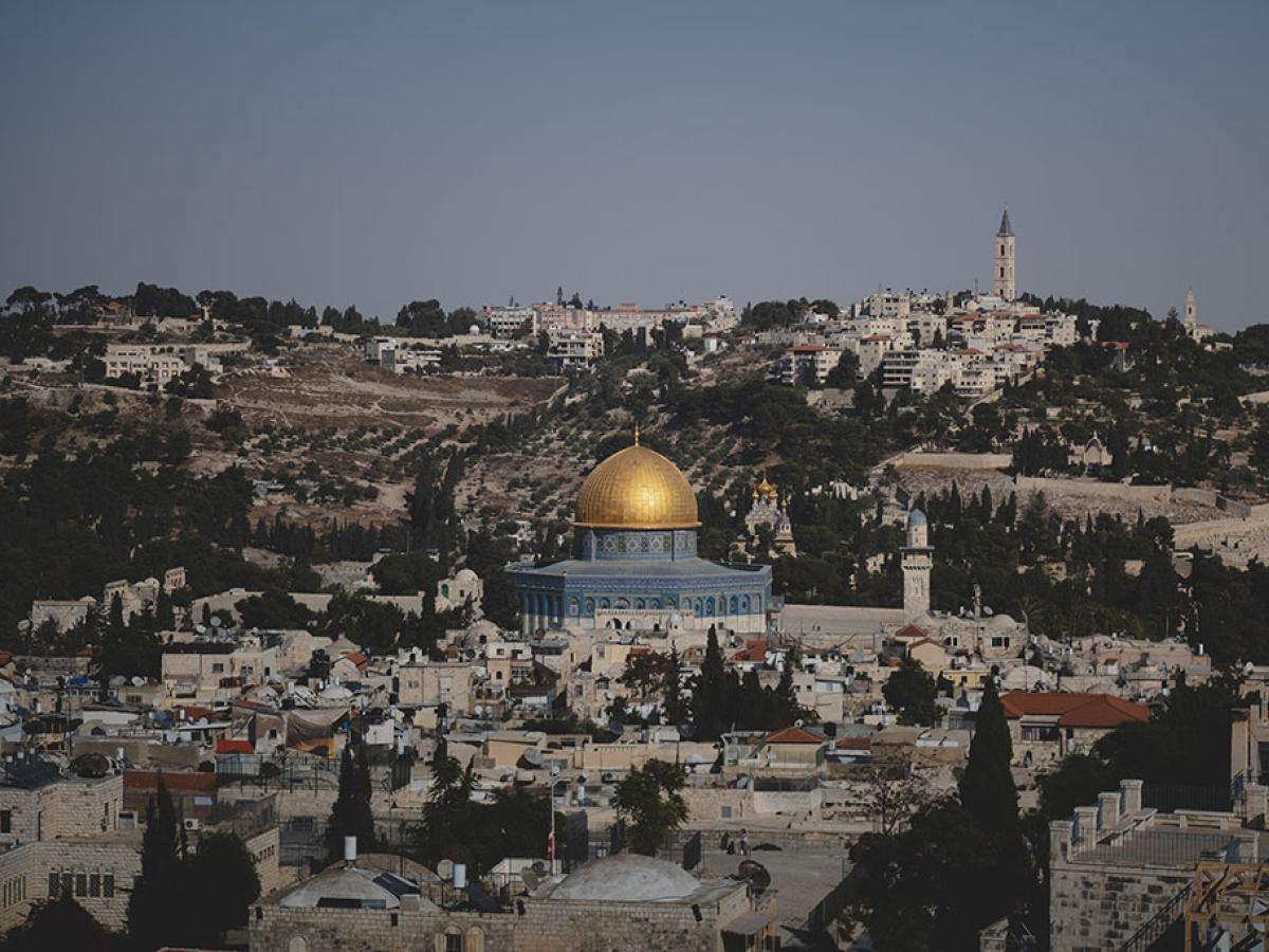 A blue and gold domed mosque sits surrounded by old stone buildings of a city.