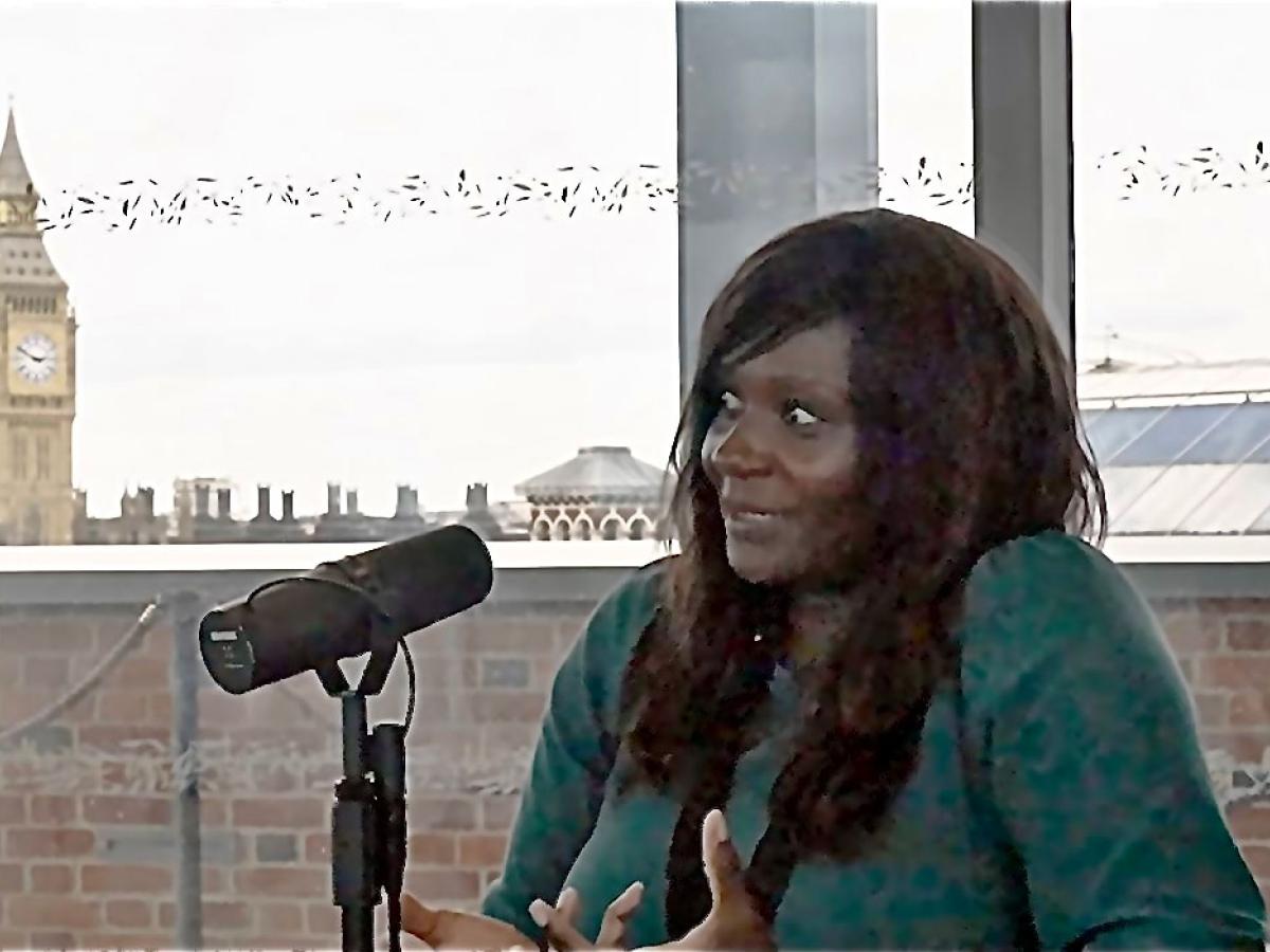 A women sits in beside a microphone taking.