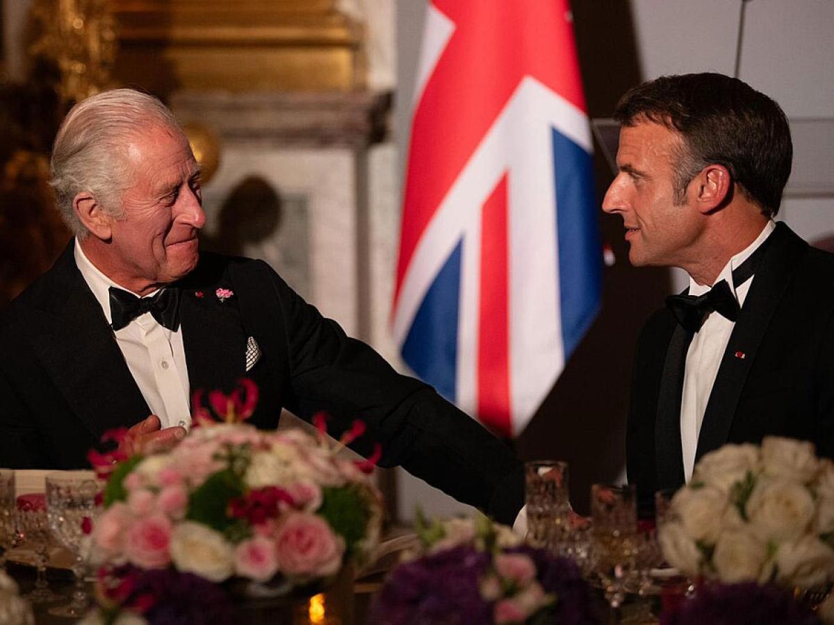 King Charles in a black dinner suit talks and gestures to President Macron who is similarly dressed.