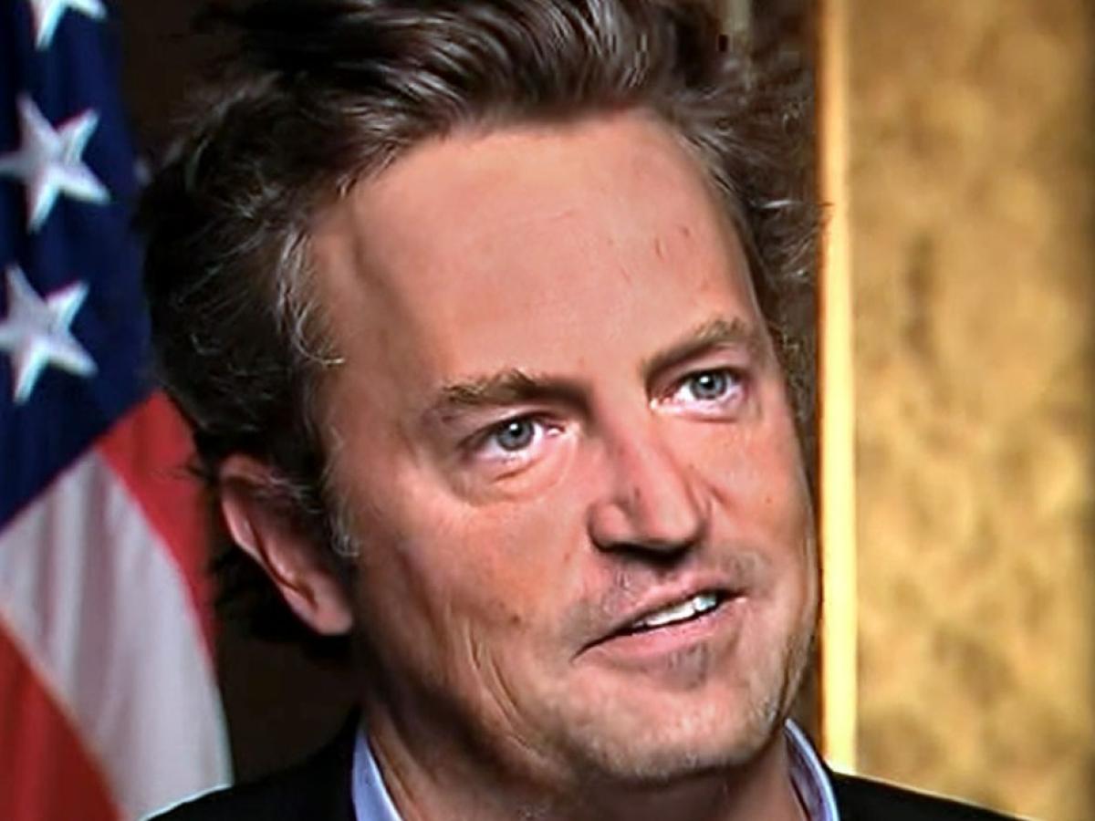 Actor Matthew Perry looks formally away, with a US flag in the background