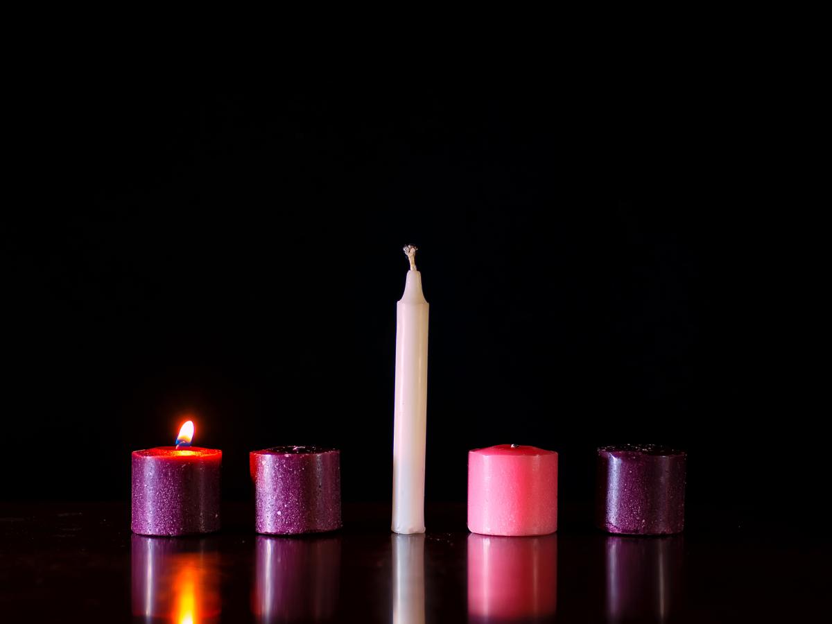 Five candles sit in a row against a dark background, only one is lit.