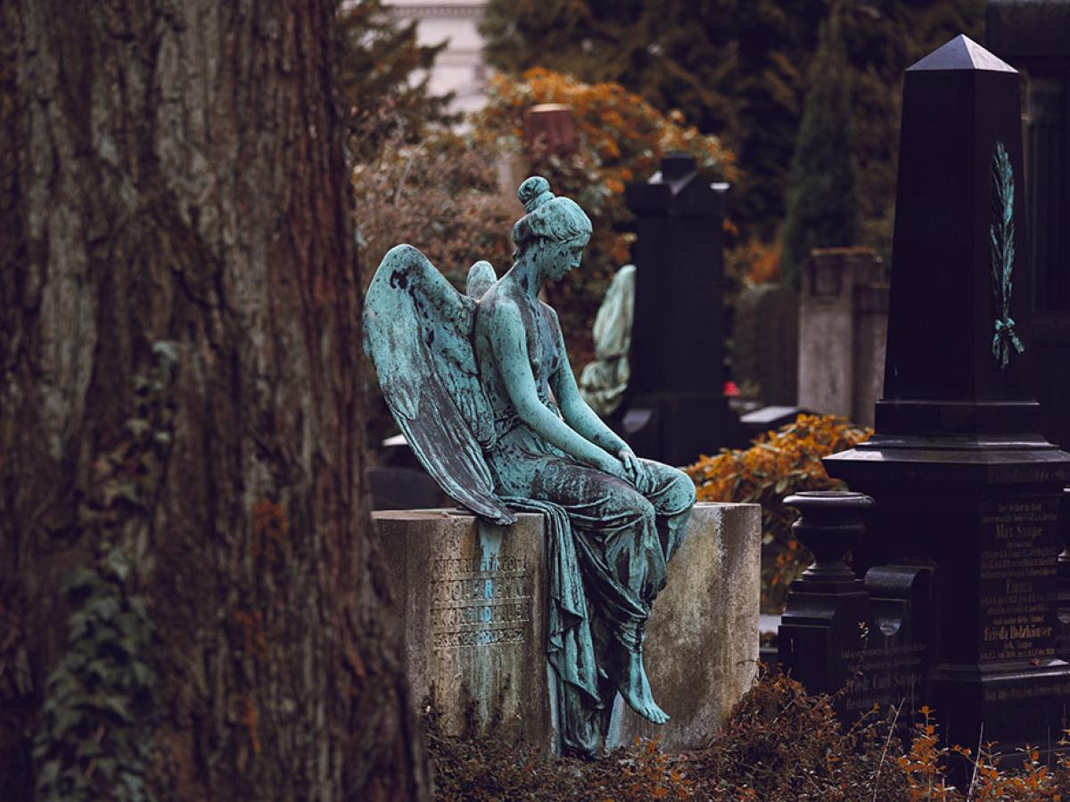 A bronze statue of a resting angel sits atop a low stone grave.