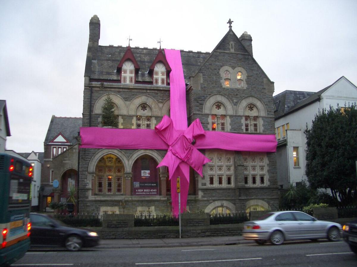 A large stone house is wrapped in a red ribbon and bow.