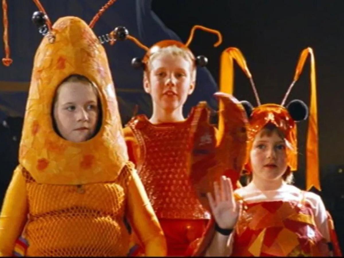 Three children dressed as orange lobsters stand sheepishly on a stage.