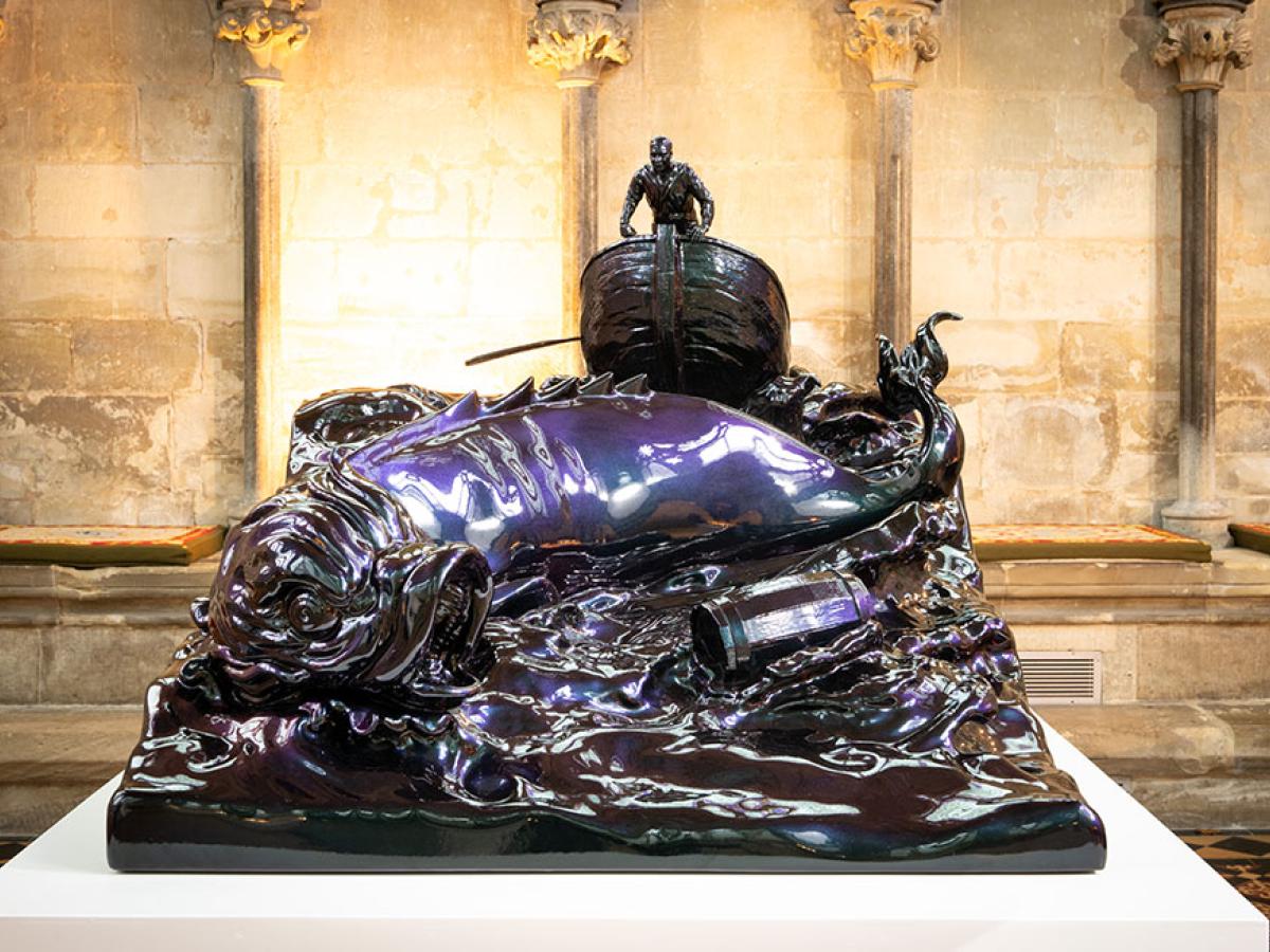 A bronze sculpture of a small boat and sea monster tossed in the waves.