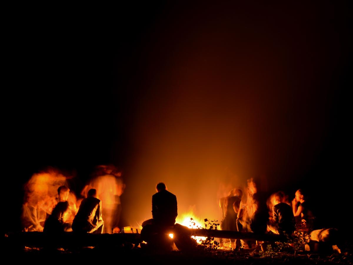 People sitting around a campfire are silhouetted against the night.