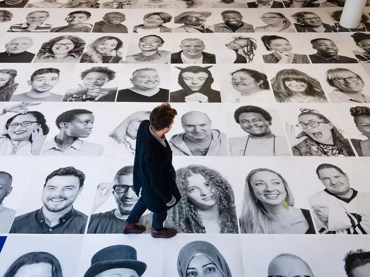 Looking down on a man walking across a grid of large black and white portrait photographs of people's faces