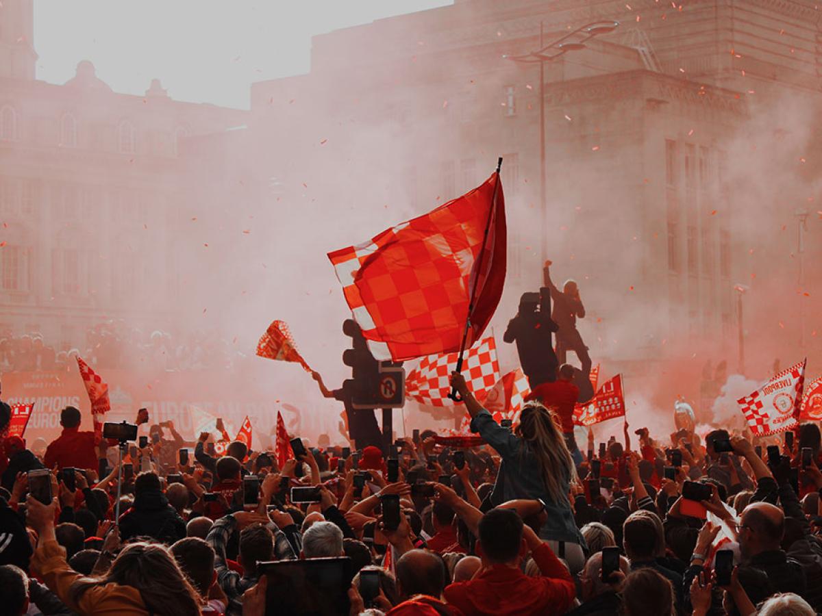 Silouhetted by red flare smoke, celebrating footballs wave red flags.