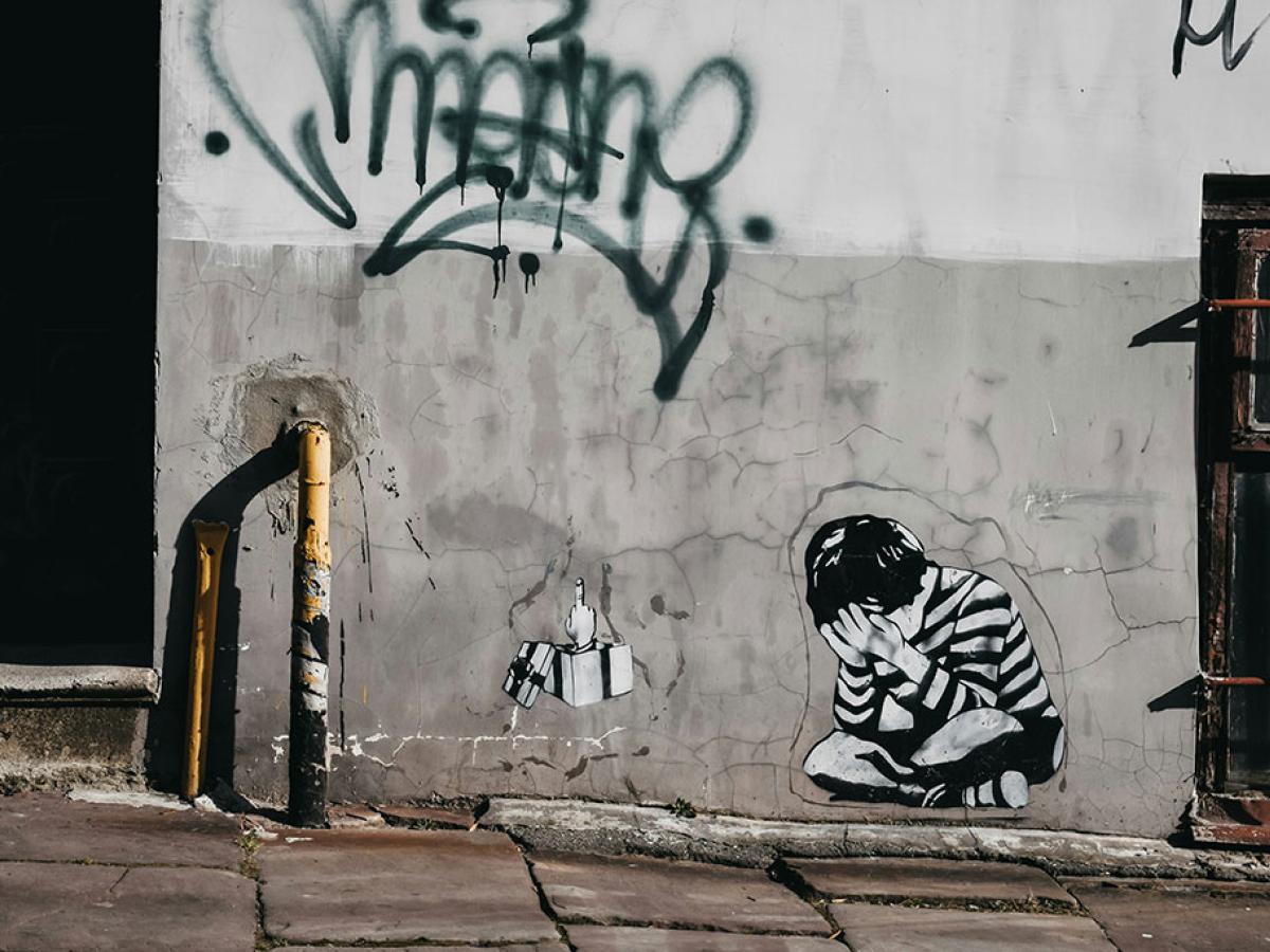 A grey and white wall graffited with a tag a image of a person crumpled and crying.