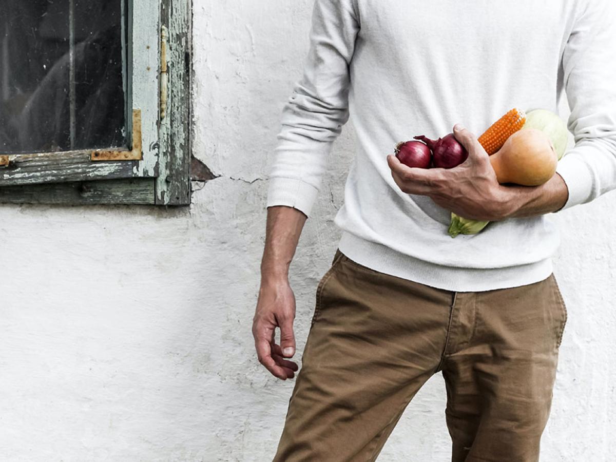 A man stands at rest, one arm holding some vegetables.