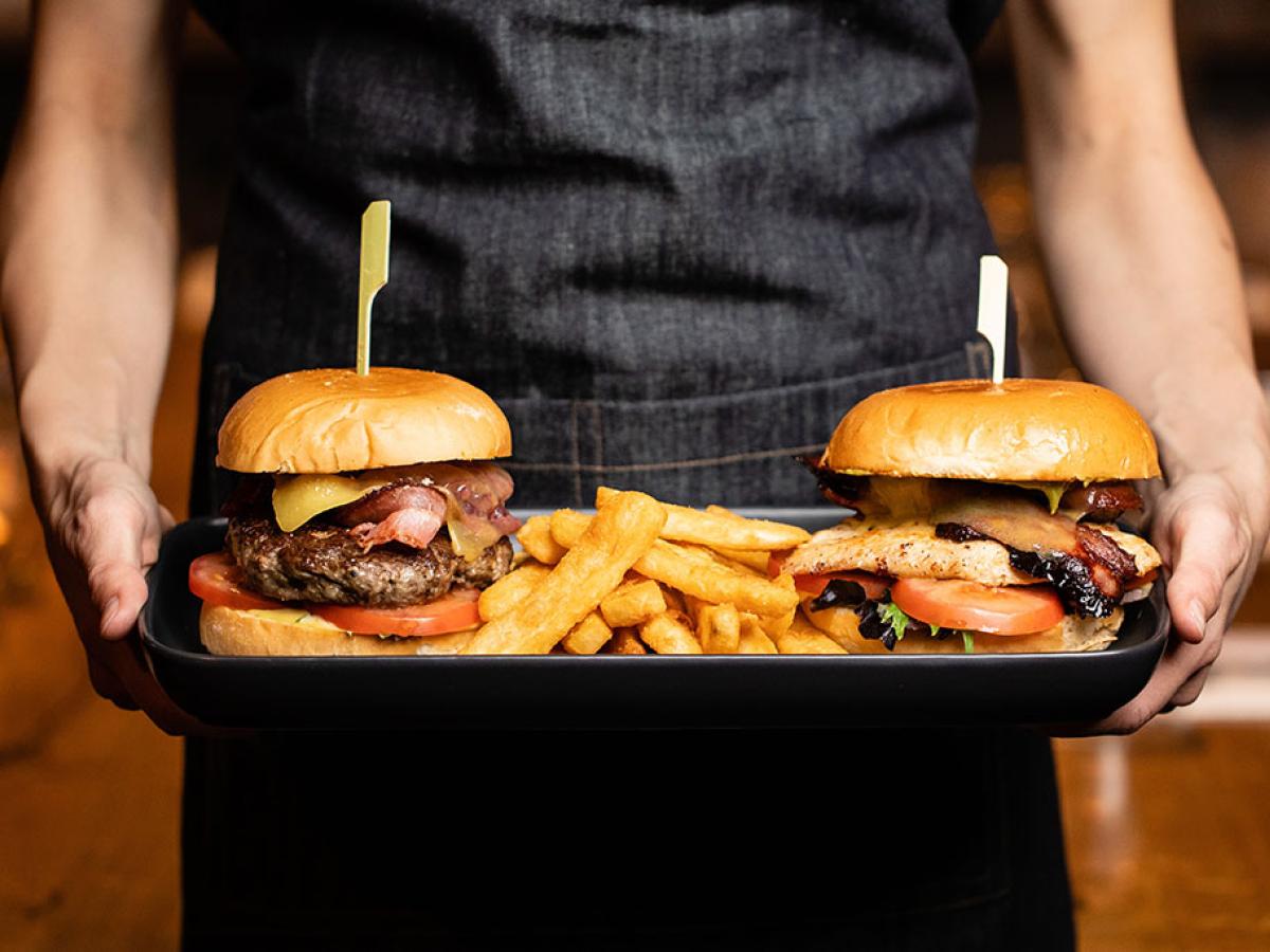 Two stuffed cheeseburgers are carried on a tray.