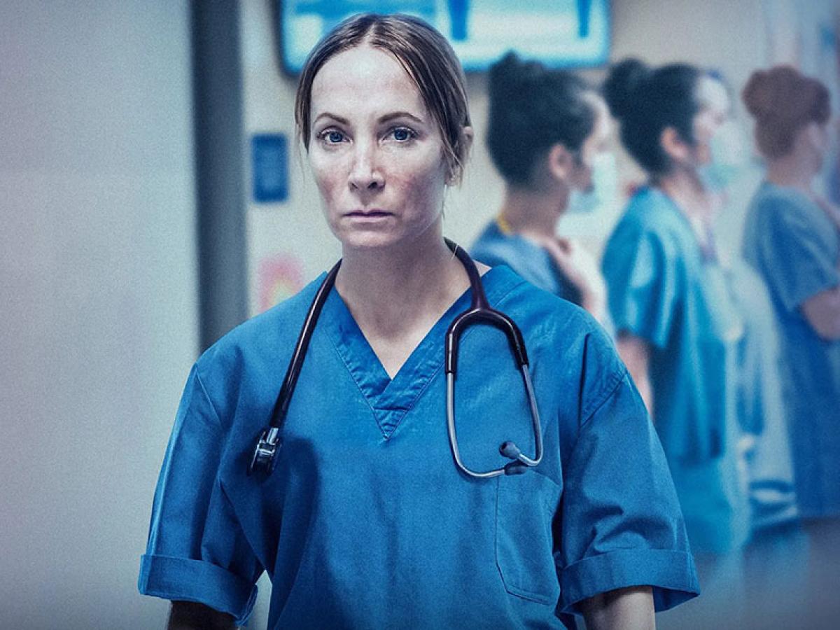 A doctor in blue scrubs stands looking exhausted.