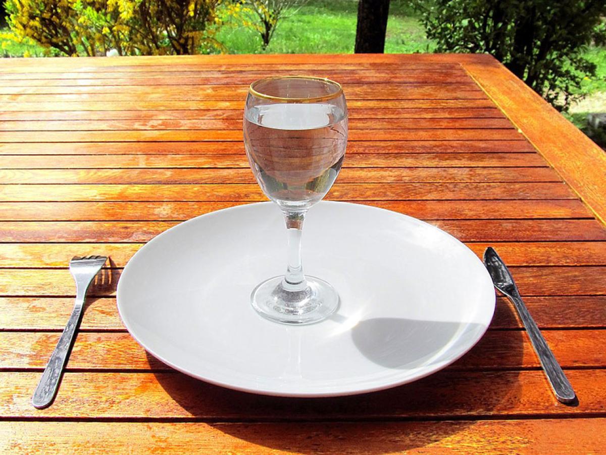 A wine glass of water sits on an empty clean plate.