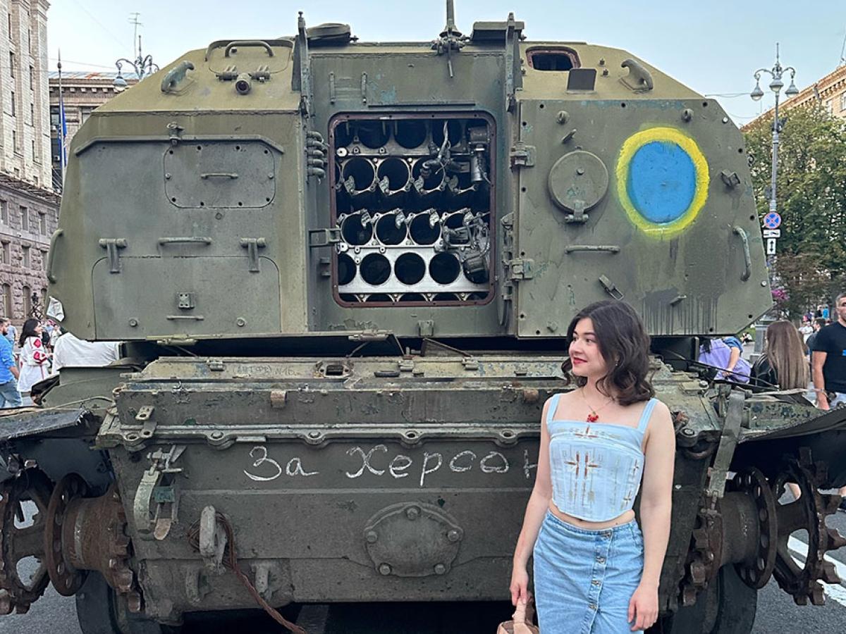 A woman stands at the back of an armoured military vehicle, the door of which is open.