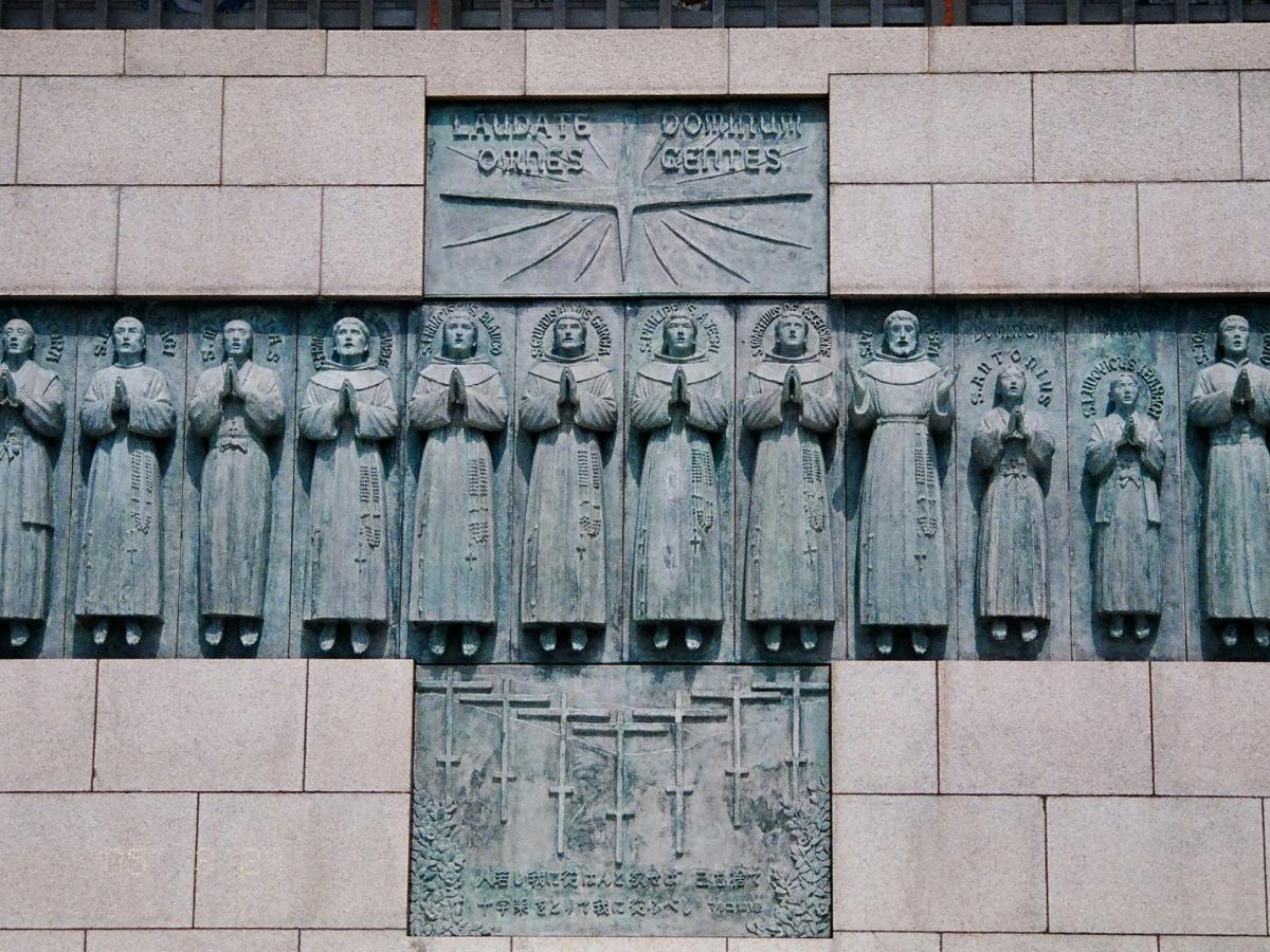 A stone monument within which set, in the shape of a cross are statues of numerous standing praying figures.