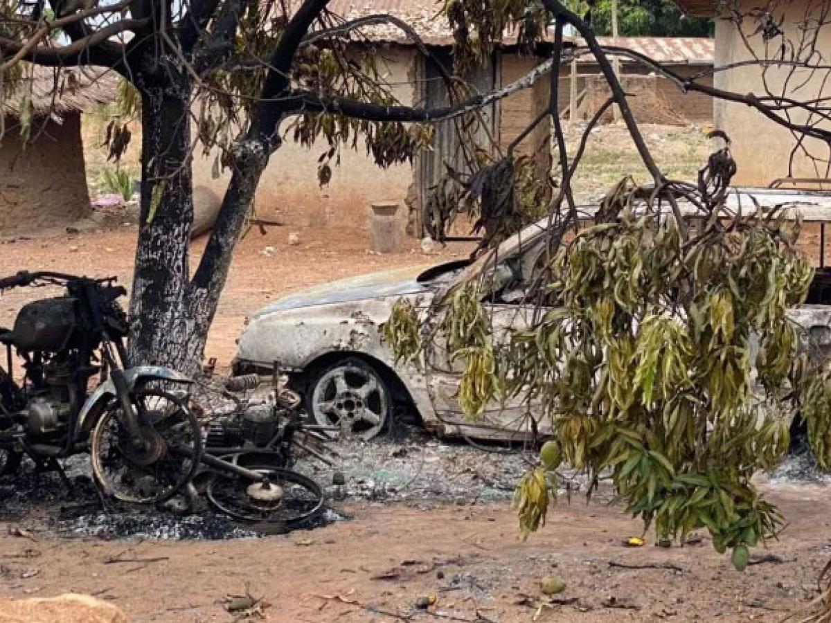 A burnt out motor cycle and car stand amid charred debris in a dusty compound.