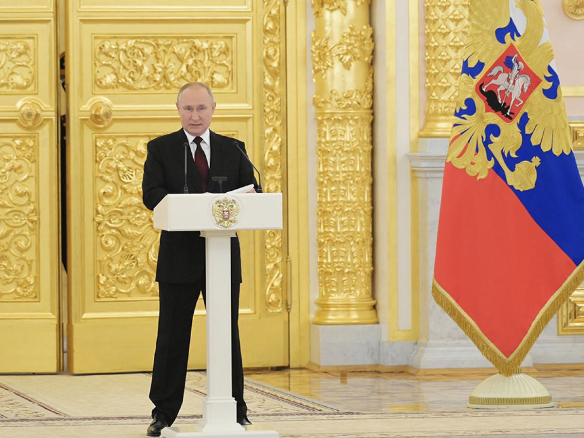 Preisdent Putin stands behind a lectern with a gold door and Russian flag behind him.