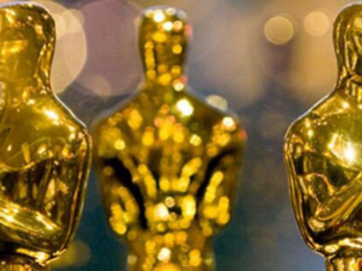 A closely cropped group of gold Oscar statues showing mostly their head and shoulders.