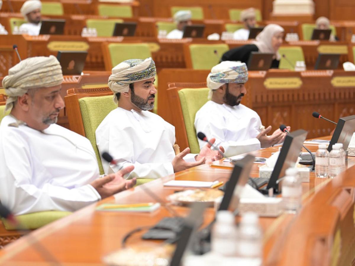 Three members of the Oman Shura sit in it's chamber and hold their hands in prayer