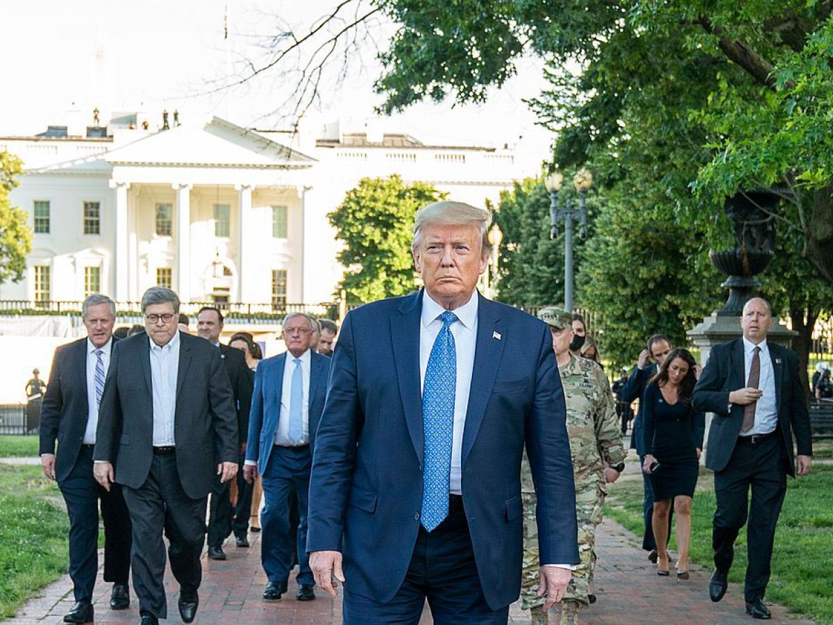 A fierce looking man walks at the head of a phalanx of suited men.