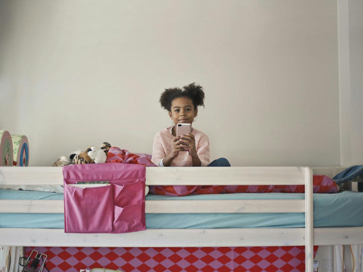 A child sits atop a bunk bed holding a phone in front.