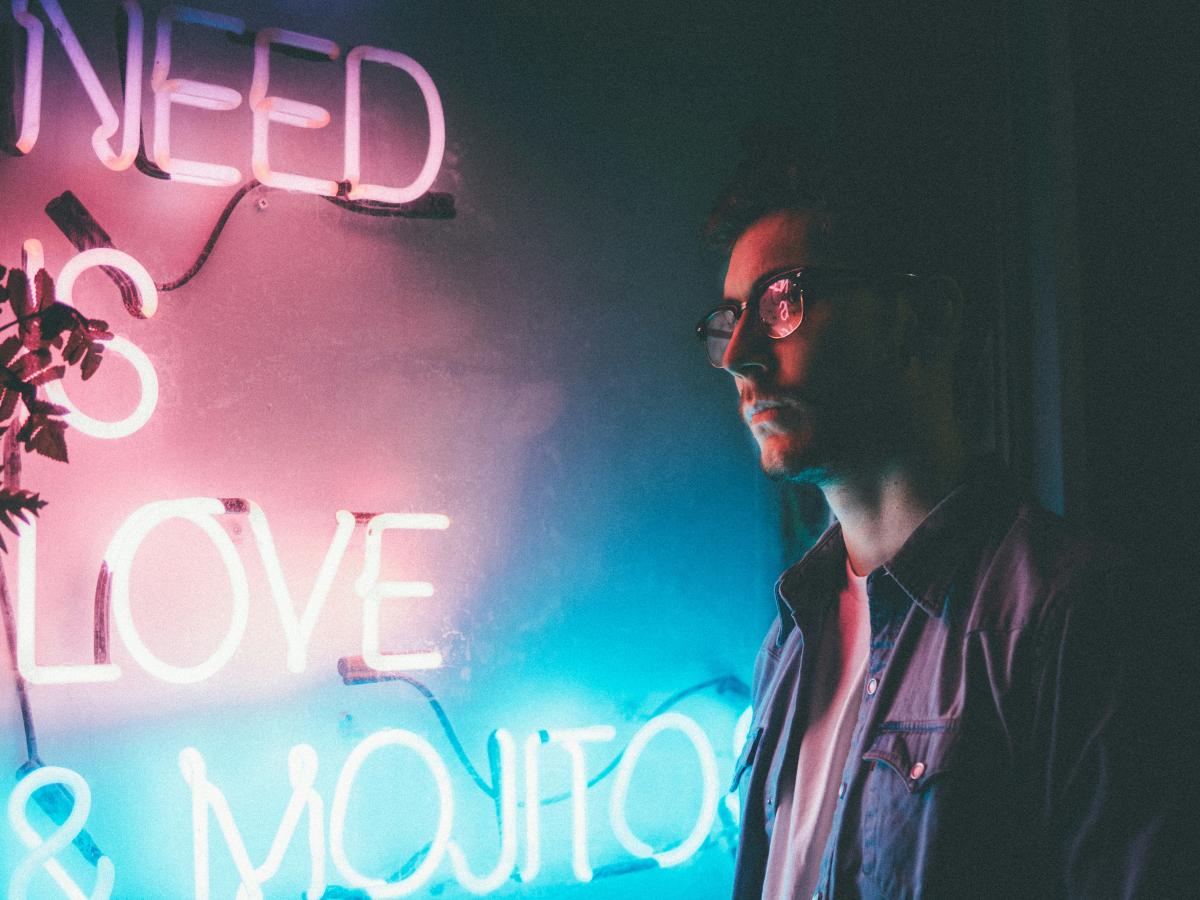 A man stands and looks at a neon sign reading 'need love and... '