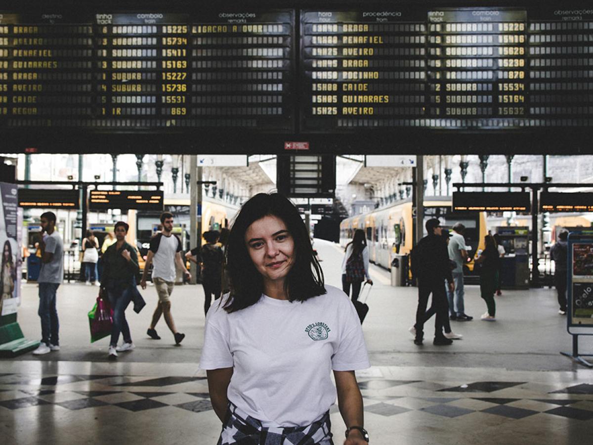 A young person stands in front of railway station platfrorms and below a large informaton display.