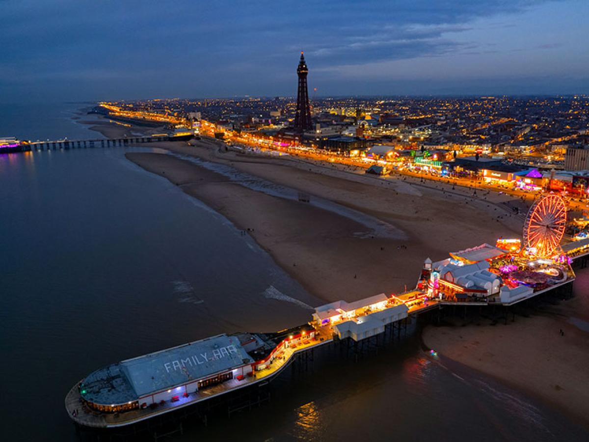 An aerial view at dusk of a brightly lit pier and promenade of the seaside town of Blackpool