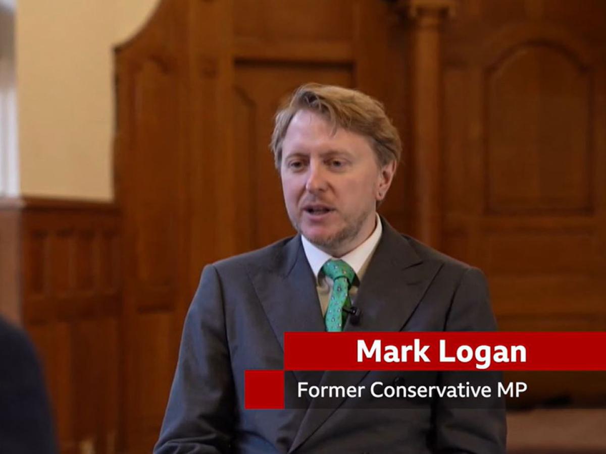 A man sits in a TV interview, below him is a captions stating 'Mark Lognan. Former Conservative MP