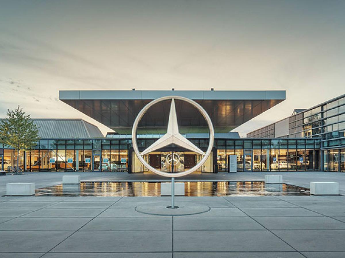 A large sculpture of the Mercedes Benz three-point star stands in front of a large, low glass fronted showroom.