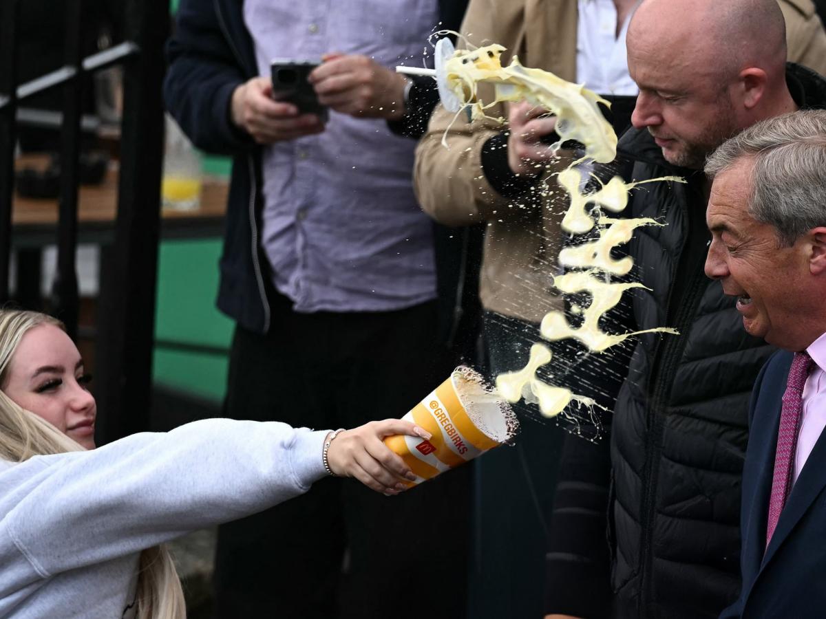 A woman throws a milkshake at a politician, the milk is mid-flight in a curved shape.