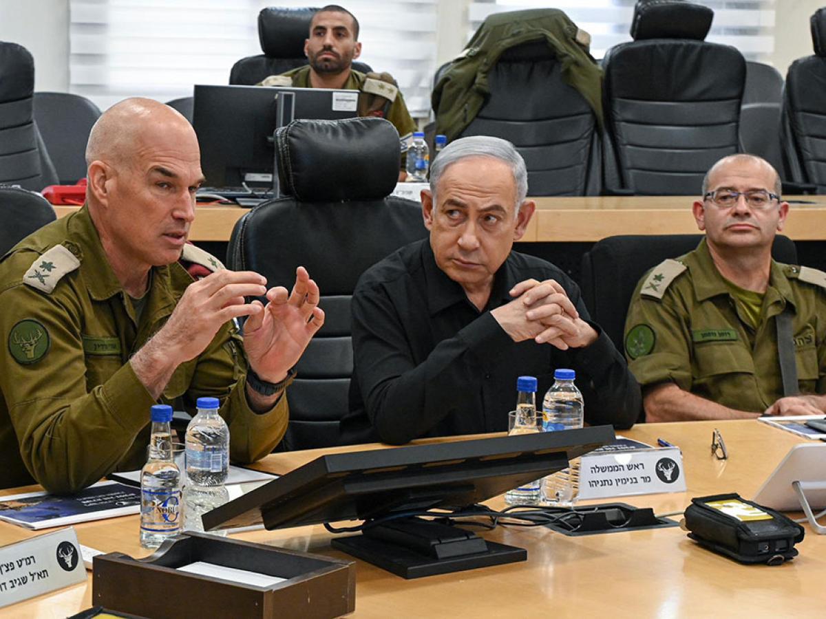 Between two generals wearing camouflage uniforms, a man in a black shirt listens.