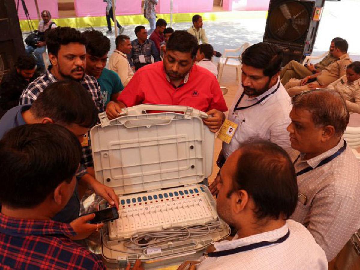 official surround an open case containing an electronic voting terminal and cables.